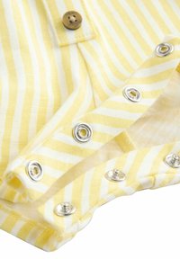 Tissu rayé jaune et blanc avec des boutons-pression métalliques et un bouton marron, montré partiellement ouvert.