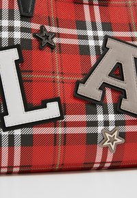 Tissu à carreaux rouge et noir avec de grandes lettres « L » et « A » cousues, ainsi que deux patchs en forme d'étoile superposés en noir et gris.