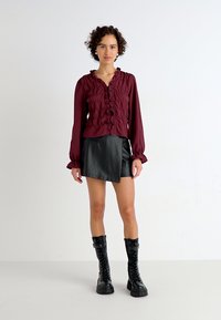 Μαρουλί μπλούζα με φρουφρού και μακριά μανίκια, συνδυασμένη με μαύρη φουστάνι από τεχνητό δέρμα και μαύρες χοντρές στρατιωτικές μπότες με διακοσμητικές λεπτομέρειες.