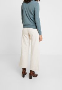 Lichtblauwe trui, beige wijde broekspijpen en bruine enkellaarsjes met hak. De broek heeft een geribbelde zoom en zakken.