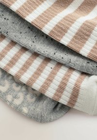 Stapel van vier opgevouwen gebreide sokken met beige en witte strepen, grijs met zwarte spikkels, en grijs met beige hartpatronen.