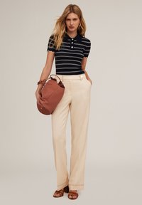 Polo rayé bleu marine avec patte de boutonnage, associé à un pantalon large crème. Portant un sac en cuir texturé marron ; chaussée de sandales à talons marron.