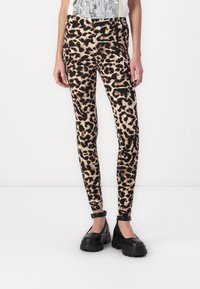 Leggings z leopardjim vzorom v bež in črni barvi, prilegajoč dizajn z gladkim in raztegljivim materialom. Nosi se z črnimi platform škornji z gležnjenčkovimi trakovi.