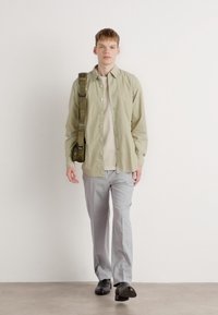 Camisa abotonada de un verde oliva claro, blusa beige, pantalones gris claro, zapatos negros, bolso de hombro. Diseño sencillo y paleta de colores neutros.