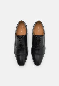 Une paire de chaussures oxford formelles en cuir noir avec un laçage fermé et des orteils carrés, vues de dessus sur un fond blanc.