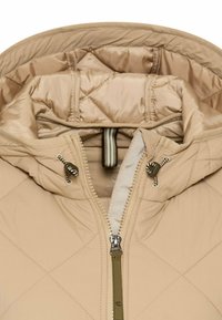 Polstret beige jakke med hætte, prydet med et diagonalt quiltet mønster, frontal lynlås og snøre detaljer. Glat, letvægtsmateriale.