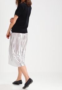 Svart kortärmad skjorta i kombination med en silverfärgad plisserad midikjol och svarta ballerinas, som visar en jämn textur och elegant design.