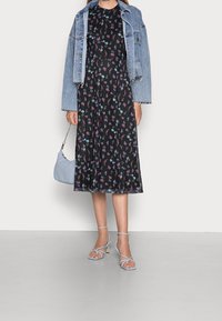 Schwarz-weißer Midi-Kleid mit floralem Druck in Blau und Pink, kombiniert mit einer cropped Jeansjacke. Hellblaue Handtasche und Riemchensandalen.