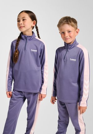 Lila Sportanzüge mit Viertelreißverschluss-Oberteilen, rosa Ärmeldetails und weißen Chevron-Mustern auf den Ärmeln, gefertigt aus einem glatten Stoff.