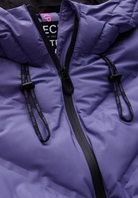 Fialová péřovka s černým zipem, na stažení a saténovým povrchem. Obsahuje značkovou nášivku uvnitř oblasti límce.