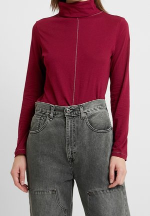 Top burdeos de mangas largas con cuello alto y costuras plateadas; combinado con pantalones de mezclilla grises de tiro alto con bolsillos tipo parche.