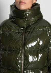 Grøn pufferjakke med høj krave, der har en blank finish, kviltet design og en lynlåslukning fortil.