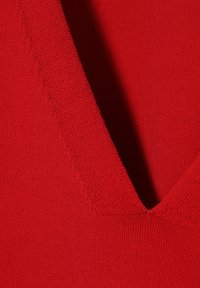 Punainen kangas, jolla on sileä rakenne ja voimakas V-pääntie. Saumojen yksityiskohta näkyy reunoilla.