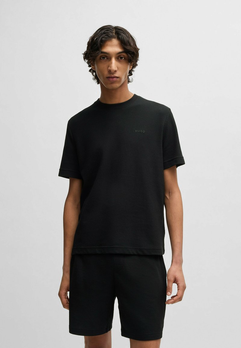 Zwarte T-shirt met korte mouwen, een gestructureerd patroon, ronde halslijn en een geborduurd logo op de borst, gecombineerd met bijpassende shorts.