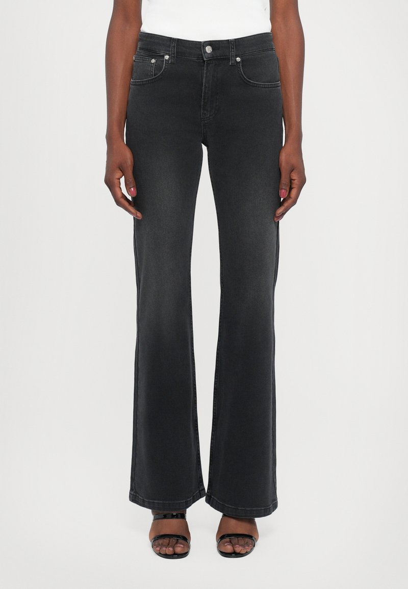 Jeans de mezclilla negros acampanados con una cintura ajustada, bolsillos delanteros y traseros, herrajes de plata y una textura suave.