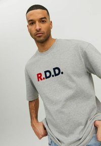 Šedé bavlnené tričko so skratkou "R.D.D." v červenej a námorníckej modrej farbe. Tričko má voľný strih a krátke rukávy.