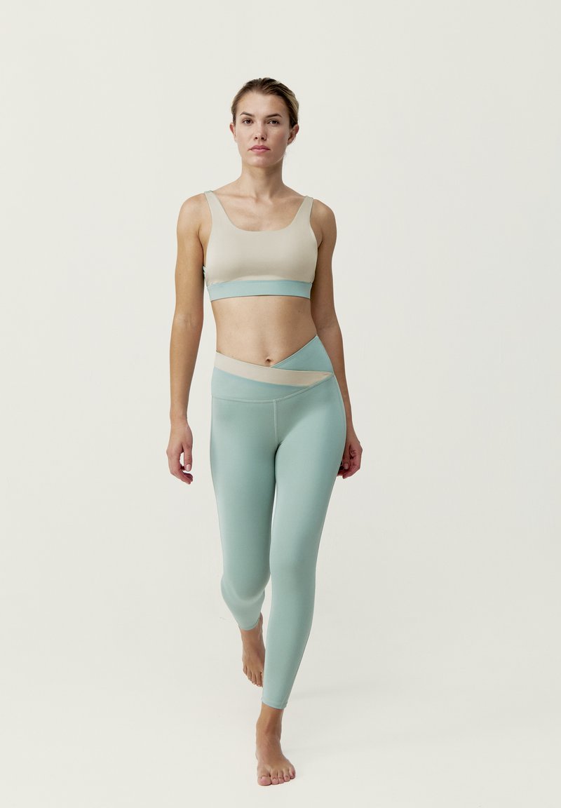 Lättvikts, sömlös träningsklädsel i beige och mintgrön. Bh:n har en rundad halsringning; leggingsen har en asymmetrisk midja.