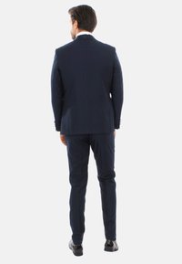 Completo blu navy con fit su misura, caratterizzato da una singola fessura, pantaloni abbinati e scarpe nere lucide, visto da dietro.