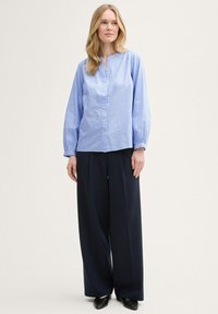 Chemise bleu clair à boutons avec un col rond et des manches froncées, associée à un pantalon large bleu marine. Motif simple et texturé visible.
