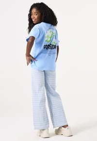 Camiseta de algodón azul claro con gráfico floral y texto en la parte posterior, combinada con pantalones de pierna ancha de patrón azul claro y zapatillas de color crema.