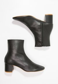Botines de cuero negro hasta el tobillo con punta afilada, tacón medio en bloque y cremallera lateral. Textura lisa y diseño minimalista.