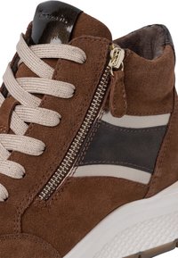 Baskets en daim brun avec des lacets beige, fermeture éclair sur le côté, rayure noire et grise, et semelle texturée blanche.