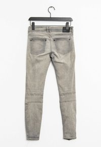 Šedé skinny džíny z denimu zavěšené na černém ramínku, s dvěma zadními kapsami a bledým, strukturovaným povrchem.