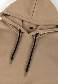 Bež kapuutsiga särk mustade nööridega, millel on hõbedased metallotsad. Pehme tekstuur, suuruse silt "M" nähtav kaeluses.