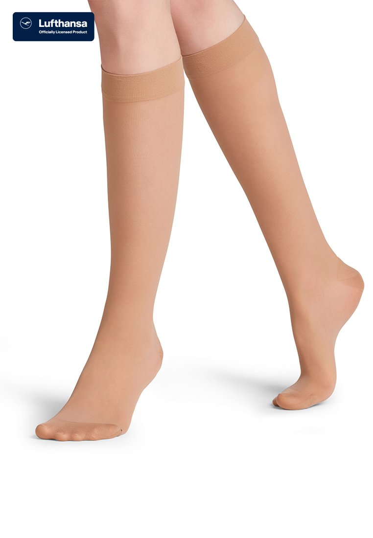 Jambes portant des bas de compression couleur chair jusqu'aux genoux, un pied à plat et l'autre légèrement relevé sur les orteils.