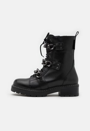 Botte de combat en cuir noir avec semelle épaisse, fermeture à lacets à l'avant et trois brides décoratives en chaîne argentée sur le dessus.