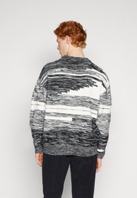 Maglione lavorato a maglia con un motivo astratto in bianco e nero, scollatura rotonda e polsini a coste. Texture morbida con una vestibilità rilassata.