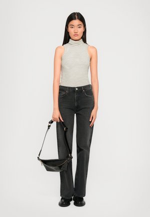 Black high-waisted jeans, fitted striped sleeveless top, carrying a black patent handbag with a strap, wearing black chunky shoes.