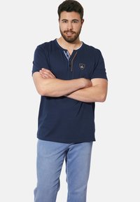 Navy blue short-sleeve polo shirt with a buttoned placket, contrast stitching, and a small embroidered logo on the chest.