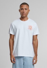 Bijela pamučna majica s ružičastim grafičkim dizajnom na lijevoj strani prsiju. Opušteni kroj s kratkim rukavima i okruglim izrezom.