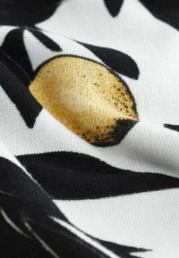 Zbliżenie czarno-białej tkaniny z żółtym i czarnym abstrakcyjnym okrągłym wzorem oraz widoczną fakturą dzianiny.