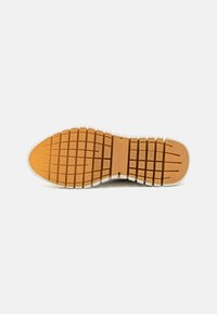 Suola di scarpe realizzata in un materiale gommoso flessibile e testurizzato di colore arancio-marrone, con un battistrada modellato per garantire aderenza e un bordo bianco.