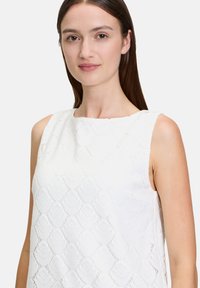 Biała bezrękawnik z teksturowanym wzorem w kształcie muszli, gładki materiał, okrągły dekolt i proste linie, ukazujący prostotę i szczegół.