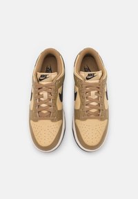 Nike tenisky s horní částí z hnědé kůže, perforovanou špičkou, černým logem Swoosh a béžovými šňůrkami na bílé mezipodešvi.