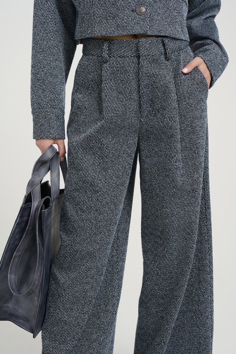 Pantaloni a scacchi grigi con una vestibilità relaxed, vita alta e tasche laterali, abbinati a una borsa a tracolla in pelle nera.