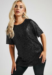 Svart paljetttopp med lös passform, korta ärmar och rund halsringning. Tyget glimmar med en strukturerad, reflekterande yta.
