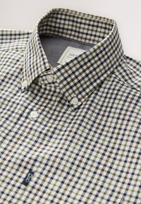 Knopfleistehemd mit einem karierten Muster in Marineblau, Braun und Creme, mit klassischem Kragen und weißen Knöpfen. Logofahne am Saum.