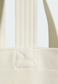 Detalj platnene torbe boje bež, s čvrstim remenima, ukrasima u križnom šavu i teksturiranim završetkom.