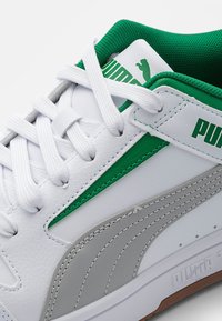Bílé tenisky s zelenými a šedými akcenty, z texturované kožené materiálu, ploché bílé tkaničky a polstrovaný zelený límec. Obsahují branding Puma.