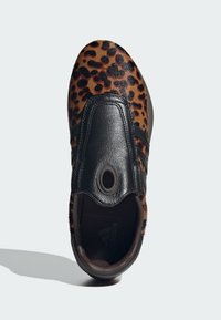 Slip-on tenisky s povrchom v leopardom vzore v hnedej a čiernej farbe, s hladkým čiernym koženým priehlavkom a oválnym výrezom pre dizajn.