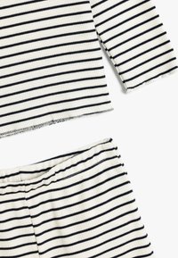 Ribbet strik set bestående af overdel og underdel i cremefarve med marineblå vandrette striber. Har en kort overdel og elastisk talje i underdelen.