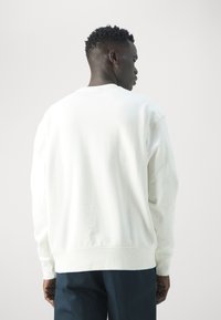 Sudadera blanca con cuello redondo, mangas largas y un corte holgado, elaborada en suave material de algodón con puños y dobladillo acanalados.