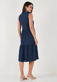 Laadun laivastonsininen, hihaton mekko, jolla on istuva bodice ja kerroksellinen hame. Rakenteellinen kangas, polven pituinen, korkea kaulus ja ei näkyviä kiinnikkeitä.
