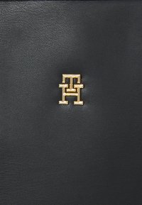 Schwarzes Lederaccessoire mit einem auffälligen goldenen Monogrammlogo. Strukturierte Oberfläche mit einem glatten, verfeinerten Erscheinungsbild.