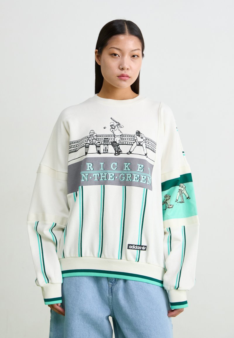 Λευκή φούτερ μπλούζα με τιρκουάζ ρίγες, γραφική εκτύπωση αθλητών του κρίκετ και κείμενο "RICKEN N-THE-GREEN". Λογότυπο Adidas κοντά στο στρίφωμα.