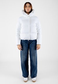 Giacca a vento bianca con colletto alto, caratterizzata da una chiusura frontale con bottoni, motivo trapuntato e maniche lunghe. Abbinata a jeans blu a gamba larga e sneakers.